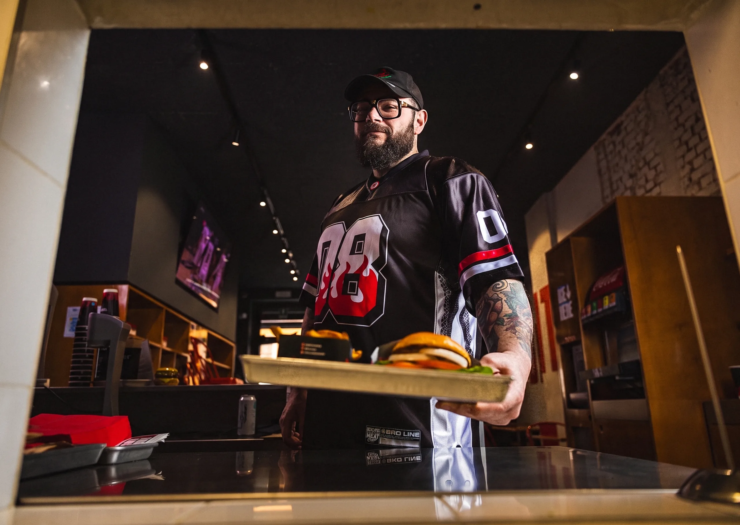 Mocho al pass di uno store Meat Crew, con la jersey 08, mentre serve un vassoio con burger e patatine