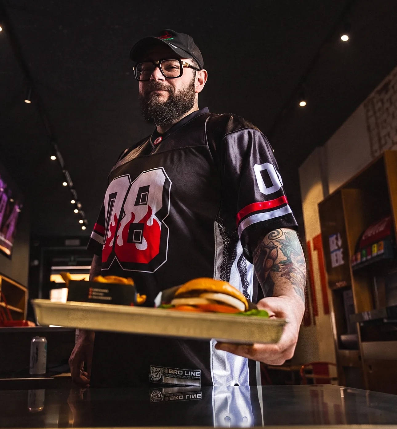 Mocho al pass di uno store Meat Crew, con la jersey 08, mentre serve un vassoio con burger e patatine